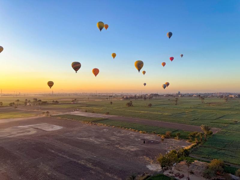 يحلّق المنطاد في سماء الفجر، كاشفًا عن إطلالة خلابة على معابد الأقصر، والصحراء ومزارع المانغو والموز./ أفضل التجارب والمغامرات في فنادق ومنتجعات العالم العربي