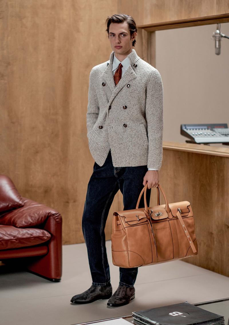 كنزة محبوكة من الصوف البكر والحرير والكشمير، وقميص من القطن، وسروال من الدنيم، وربطة عنق مشغولة من الحرير، وحذاء تشيلسي مصنوع من جلد العجول، وحقيبة Weekend Country Bag المشغولة من جلد العجول. 